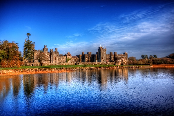 An Irish castle on a clear blue lake with blue skies overhead