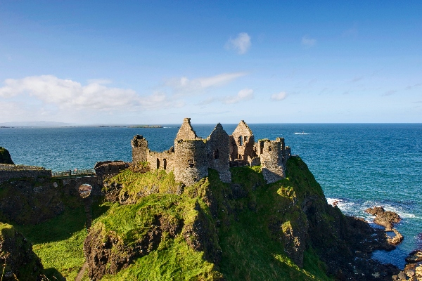 Dunluce Castle in Ireland, set atop a green cliff with the blue sea in the background