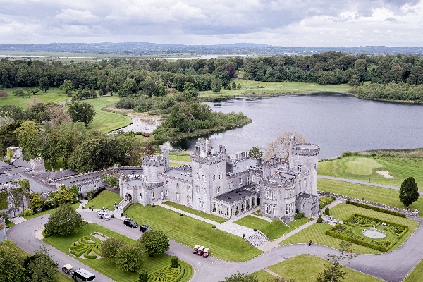 An aerial view of the Dromoland Castle Hotel in County Clare, Ireland. The building are set on a small lake with forested areas around it.